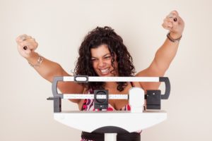Happy woman celebrating her weight loss on a medical weight scale | Luz MediSpa in Somers, NY